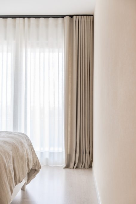 Habitación con luz natural, cortinas beige y una cama con ropa de cama clara.