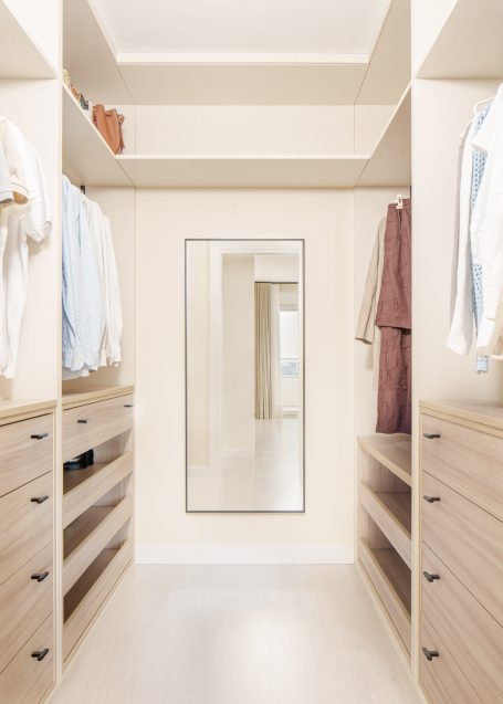 Armario espacioso con espejo, ropa organizada y estanterías de madera clara.