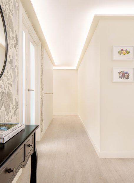 Pasillo iluminado con paredes claras y cuadros decorativos, adornado con un mueble negro.